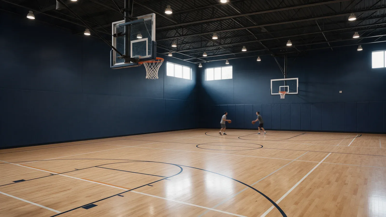 Vue depuis le bord d’un terrain de basket intérieur éclairé, avec paniers et joueurs à distance.